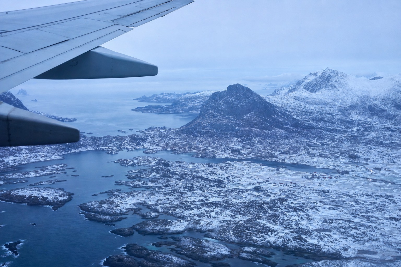 Aircraft wing above a snow-covered Norwegian coastline in low blue winter light