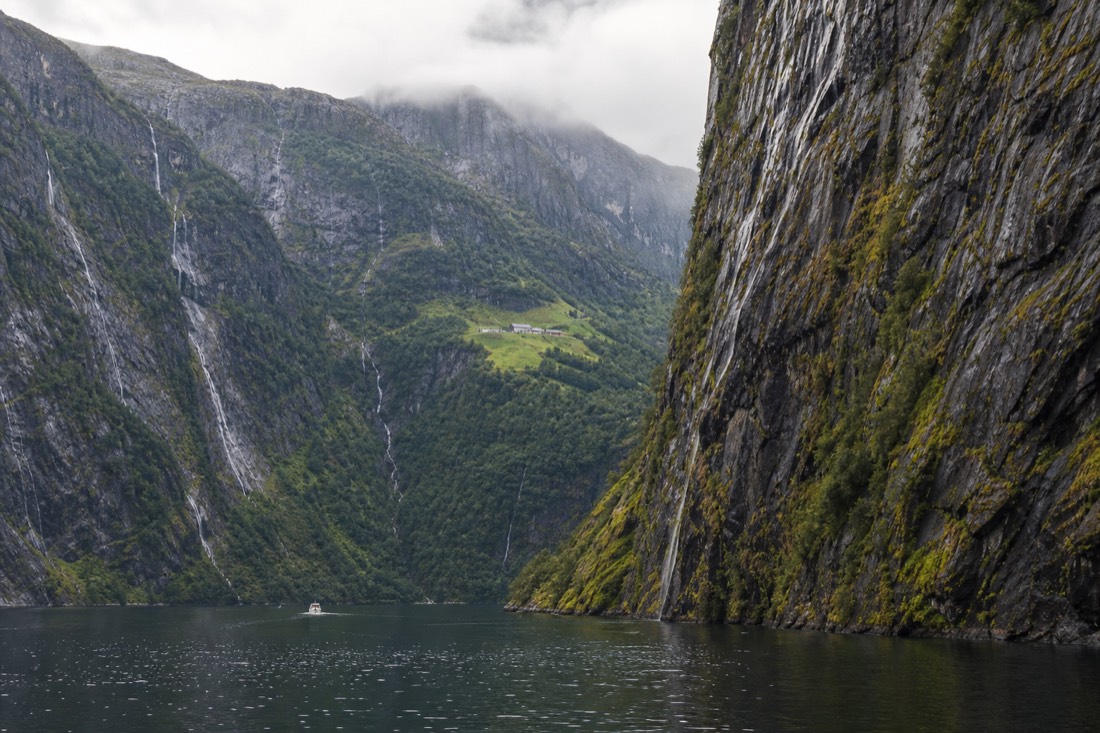 Sheer rock walls closing in on a still fjord channel with a farm on a green ledge halfway up