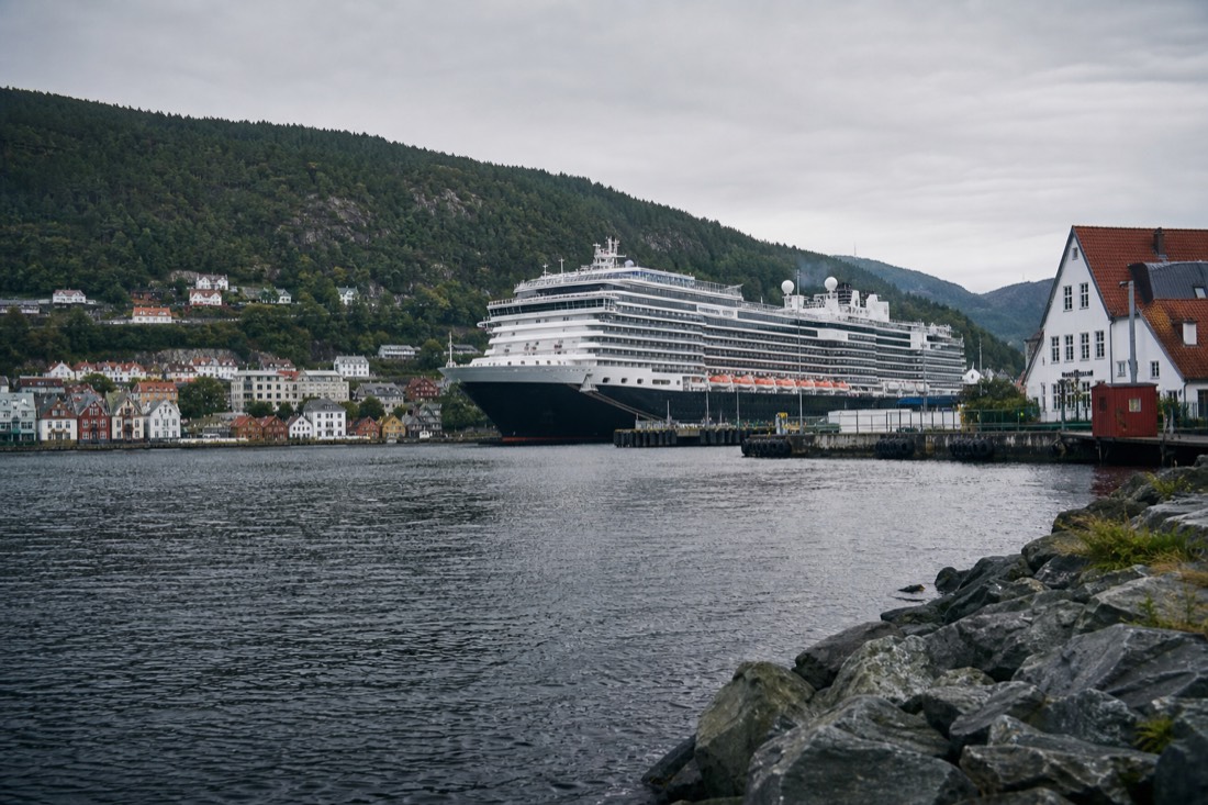 Large cruise ship berthed beside a Norwegian harbour town with wooden quays and forested hills behind