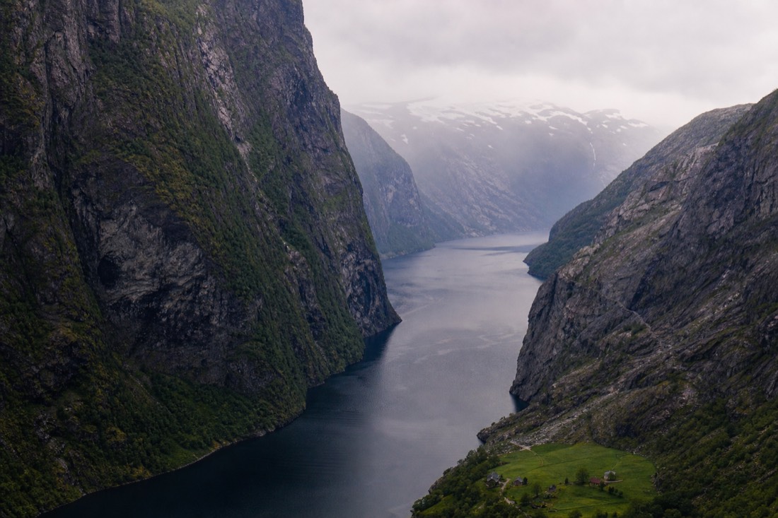A very narrow fjord arm with steep walls on both sides closing in over dark still water and a tiny farm on the shore