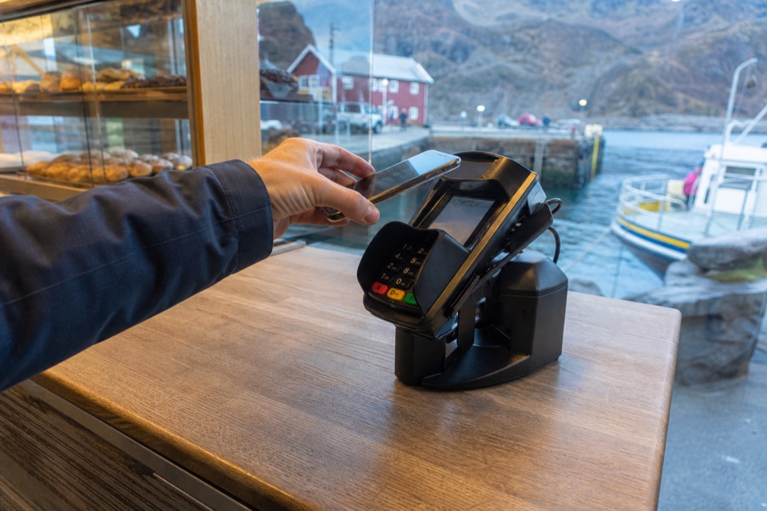 Hand holding a phone over a contactless card terminal at a small Norwegian bakery counter