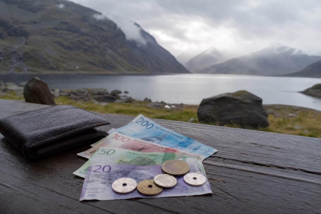 Norwegian krone banknotes and coins lying on a wooden table beside a leather wallet