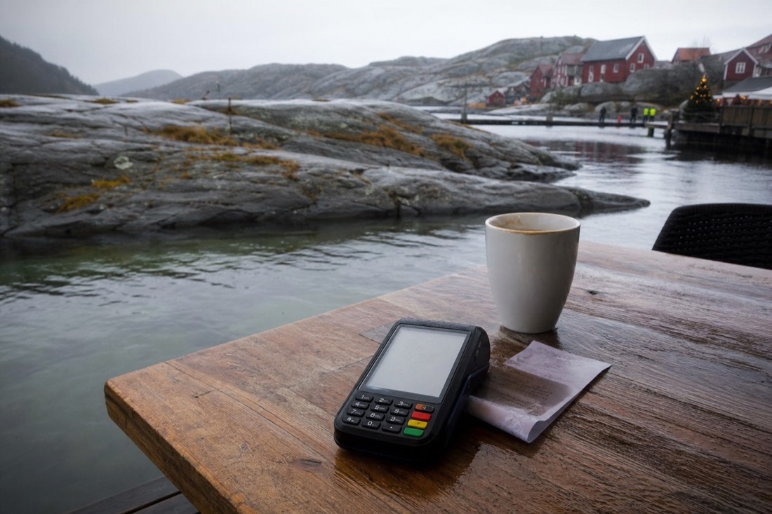 Card terminal on a wooden restaurant table beside a coffee cup and a folded paper receipt