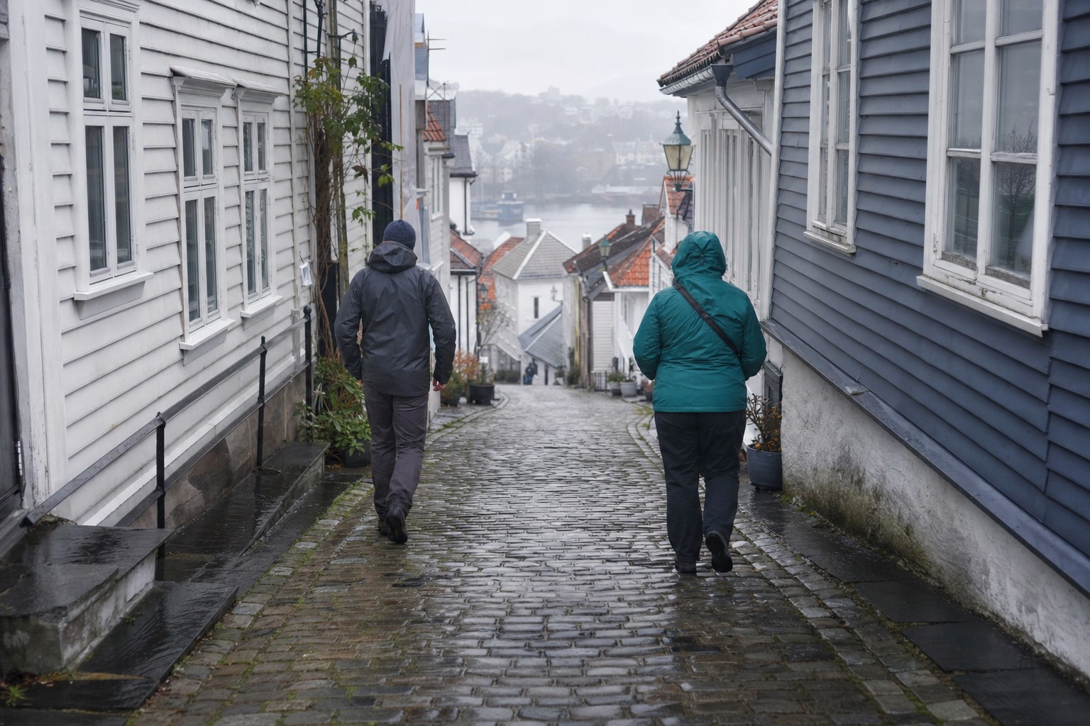 People in wool sweaters and waterproof shell jackets walking a wet cobbled street in a Norwegian city