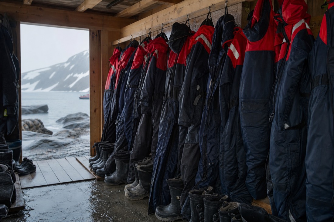 Row of insulated thermal suits and winter boots hanging ready inside an Arctic tour base