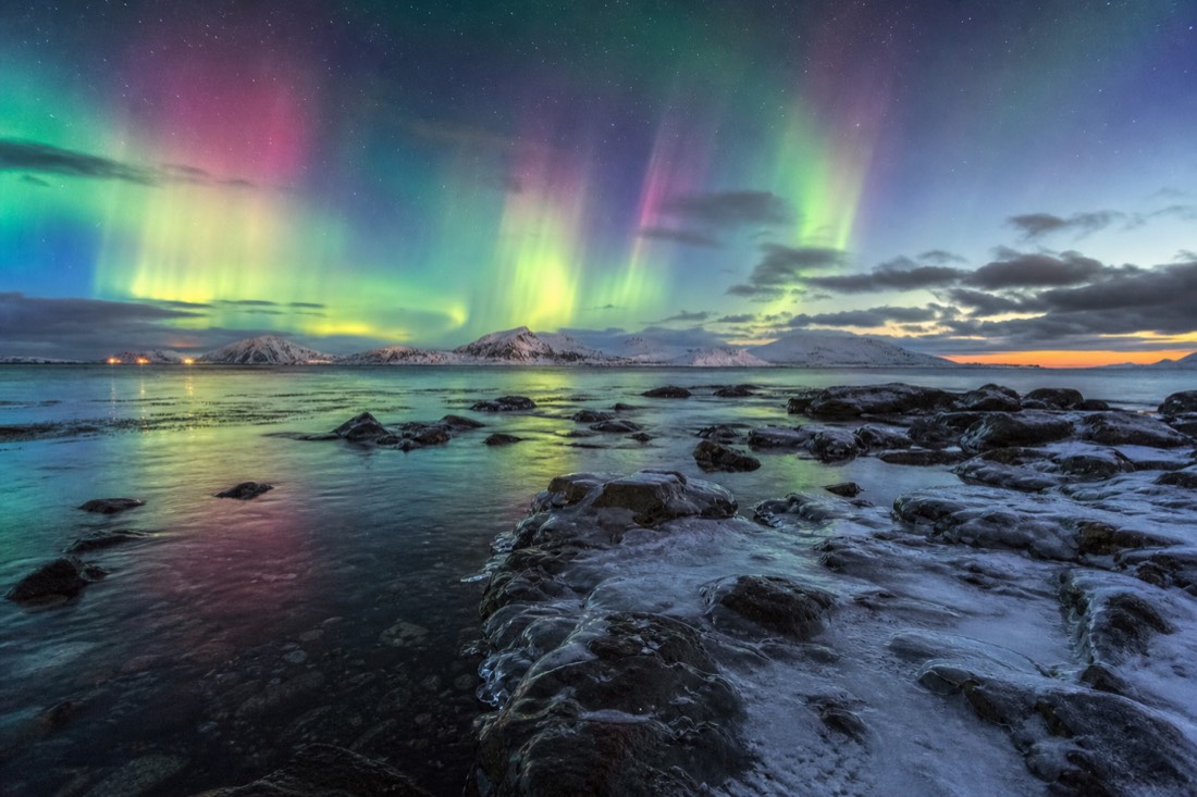 Bright multi-coloured aurora curtain filling the sky above a snow-covered Arctic shoreline