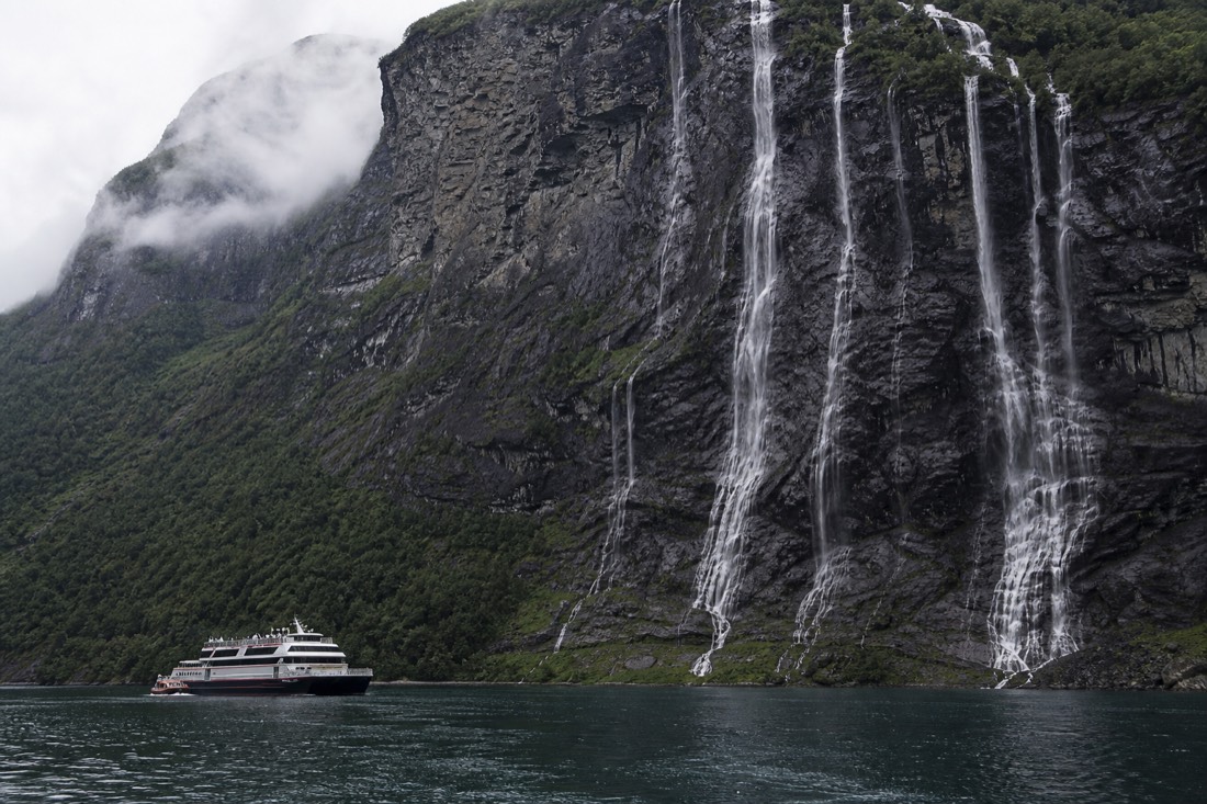 The Seven Sisters waterfall streaming down the cliff face of Geirangerfjord beside a small cruise boat