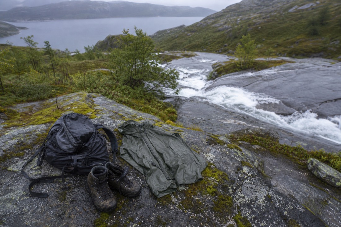 Hiking boots waterproof jacket and small backpack laid out on a mossy rock beside a Norwegian trail