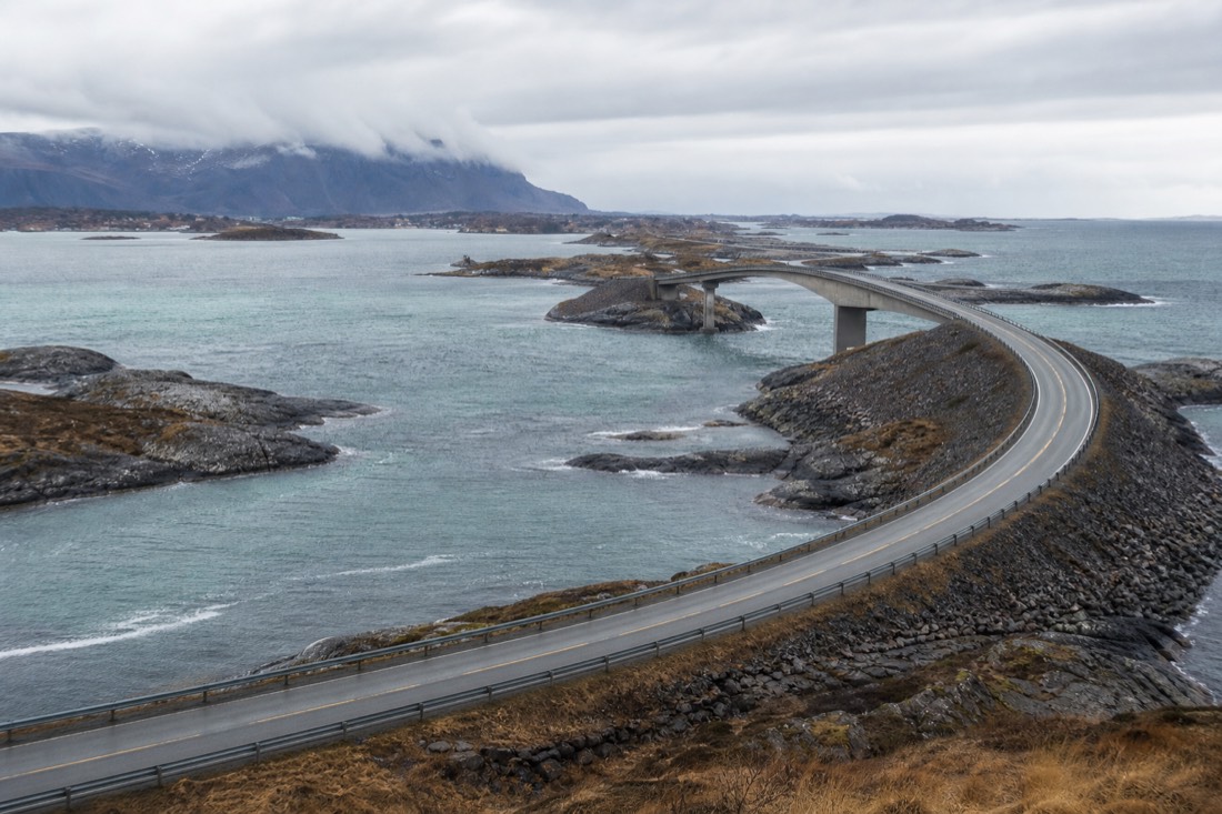 Winding coastal highway crossing a bridge between rocky Arctic islands under grey cloud