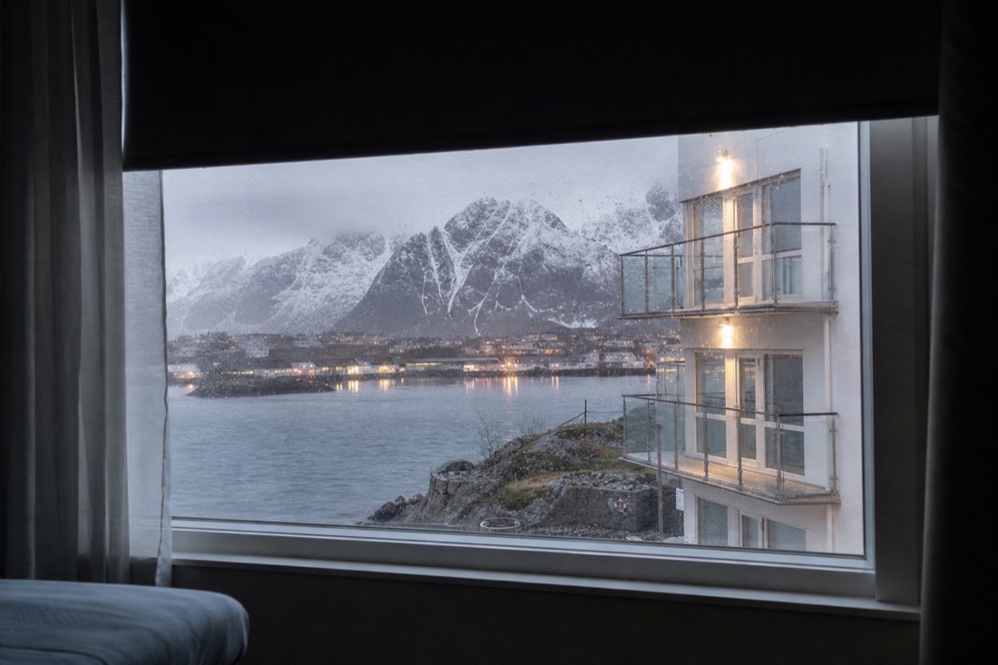 Hotel window in northern Norway with bright night light spilling past a half-drawn blackout blind