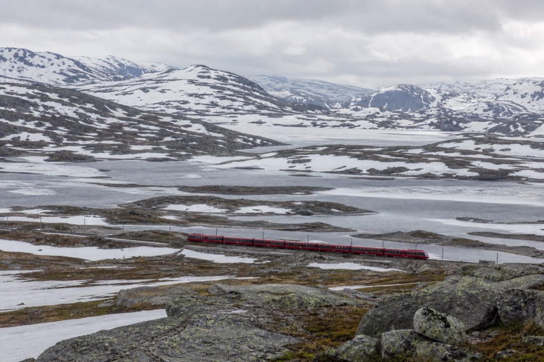 Red train crossing a snow-covered mountain plateau with frozen lakes in central Norway