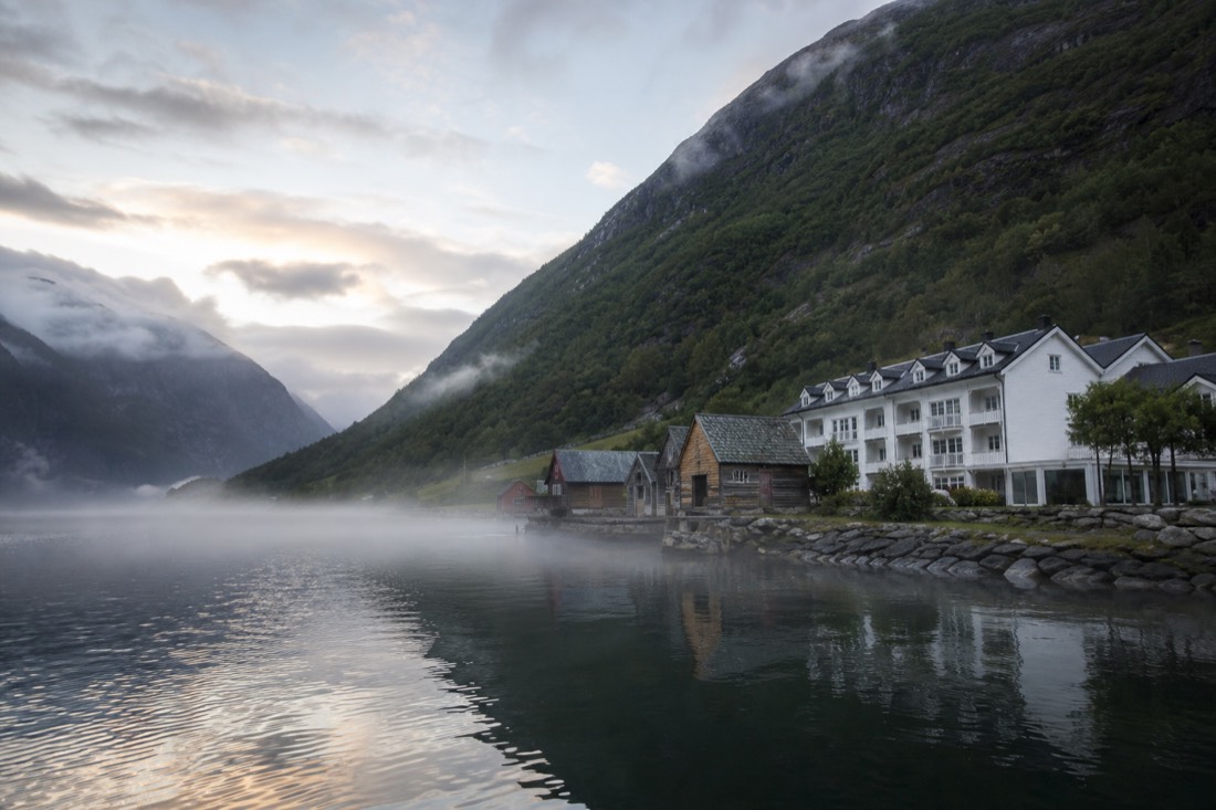 Small waterside hotel and boathouses at Flåm at dawn with mist sitting on the fjord surface