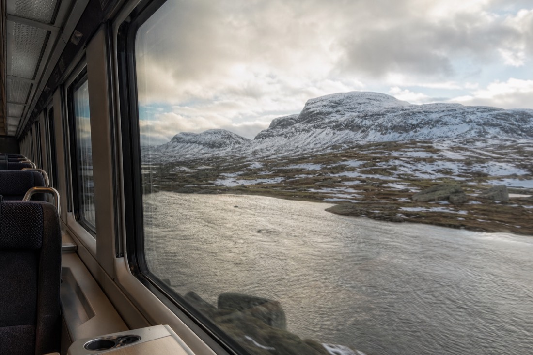 Interior of a Norwegian long-distance train carriage with wide windows framing a snow-dusted mountain plateau