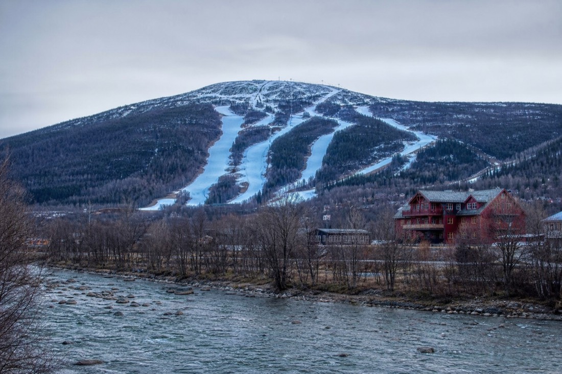 Wide view of a low forested Norwegian ski mountain with wide blue pistes and a red timber lodge below