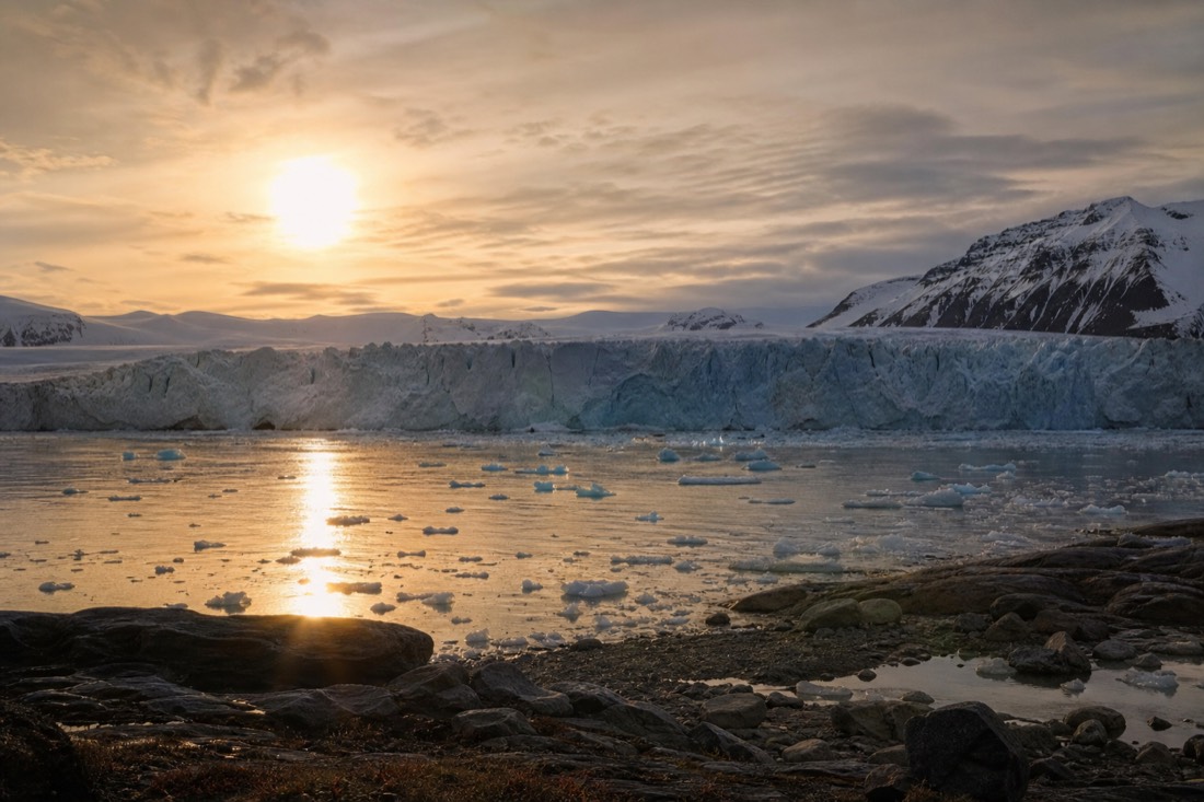 Midnight sun low over a Svalbard glacier front with calved ice floating in still fjord water