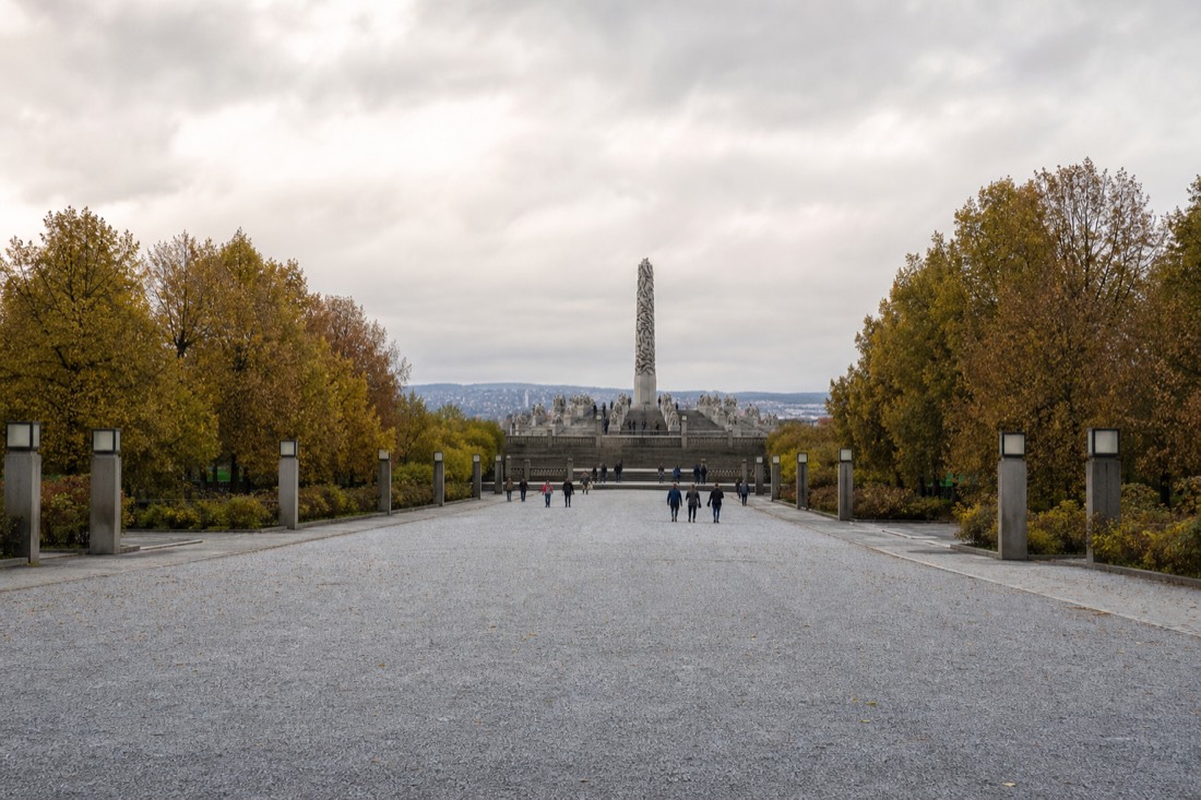 Bronze human figures on a granite plinth in a large open sculpture park with autumn trees behind