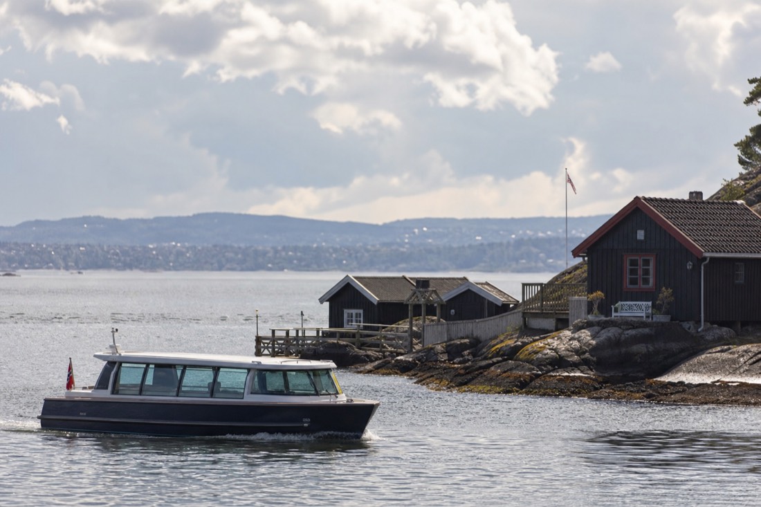 A low electric sightseeing boat gliding past small wooden island cabins on the calm inner Oslofjord